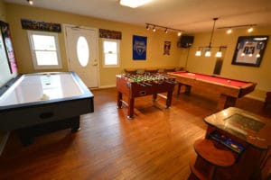A cabin game room with an air hockey table, pool table, arcade, and foosball table in a yellow room